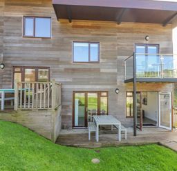 The exterior of a modern wooden building with a small patio area and balcony at Sea Breeze 17 Gannel in Porthtowan