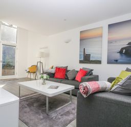 A living room with sofas red and green cushions white coffee table and large wall art at Sea Breeze 17 Gannel in Porthtowan
