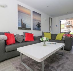A living room with grey sofas red and green cushions and a white coffee table at Sea Breeze 17 Gannel in Porthtowan