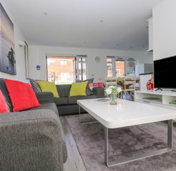 A living room with gray sofas and colorful cushions a white coffee table a television and dining table at Sea Breeze 17 Gannel in Porthtowan