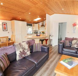 An open living room and kitchen with two sofas, a wooden dining table, and a kitchen island at Fell View Lodge in Troutbeck
