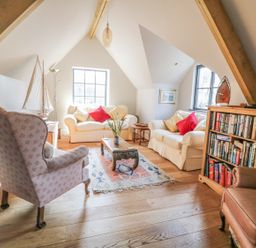 A living room with sofas armchairs a coffee table bookshelf and decorative boat at The Coach House in St Columb Major