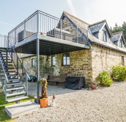 An outdoor metal staircase leading to a raised balcony attached to a stone house with gravel and plants around at The Coach House in St Columb Major