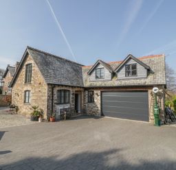 An exterior view of a stone house with a large garage and a paved driveway at The Coach House in St Columb Major