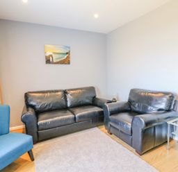 A living room with black leather sofas a blue chair a carpet a wooden cabinet and a landscape painting at The Lookout -The House With A View in Weymouth