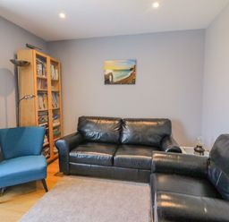 A living room with black leather sofas a blue armchair a wooden bookshelf and a wall painting at The Lookout -The House With A View in Weymouth