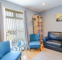 A living room with blue chairs a black leather sofa a glass side table and a wooden bookcase at The Lookout -The House With A View in Weymouth