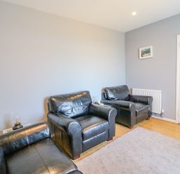 A living room with three black leather armchairs wooden floor a carpet a radiator and a door with glass panels at The Lookout -The House With A View in Weymouth