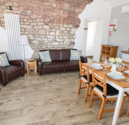 A living room with brown leather sofa and armchair next to a wooden dining table with chairs and tableware at Dairy Cottage in Tavernspite near Narberth