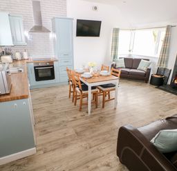 An open plan kitchen and living area with a dining table set a wood burner and sofas at Dairy Cottage Tavernspite near Narberth