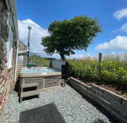 An outdoor area with a hot tub next to a stone wall and a garden with plants and a tree at Dairy Cottage in Tavernspite near Narberth