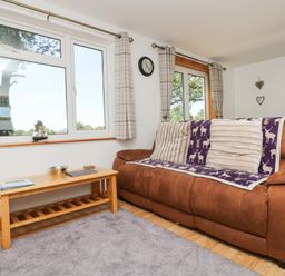 A living room with a brown sofa and a wooden coffee table by windows at Dartmoor 2 in Callington