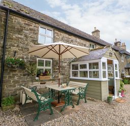 A stone cottage with outdoor seating area and umbrella at Isaacs Cottage Spartylea near Allendale