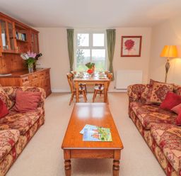A living room with two patterned sofas red cushions a wooden coffee table and a dining table with chairs at West Burnbank in Tarset near Bellingham
