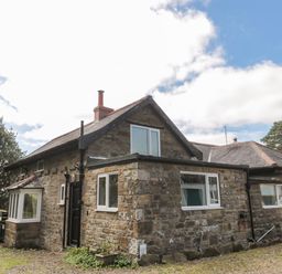 A stone house with multiple windows and a chimney under a partly cloudy sky at West Burnbank in Tarset near Bellingham