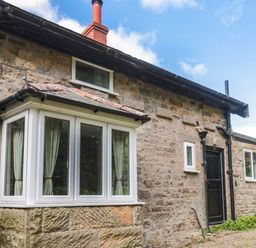 Exterior view of a stone building with white-framed windows a black door and a chimney at West Burnbank in Tarset near Bellingham