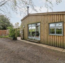 An exterior view of a wooden building with large windows and a gravel pathway at Hen House View in Rugeley