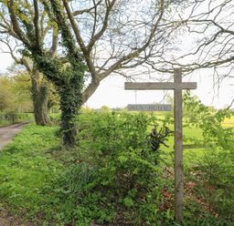 A dirt road beside a tree with a wooden sign that reads Hen House in a rural area at Hen House View in Rugeley
