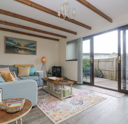 A living room with blue sofa and wooden coffee table near glass doors leading to a patio at The Lily Pad in Camborne