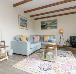 A living room with a light blue sofa and colorful cushions a wooden coffee table and a patterned rug at The Lily Pad in Camborne