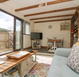 A living room with a wooden coffee table books sofa and dining table near glass sliding doors at The Lily Pad in Camborne