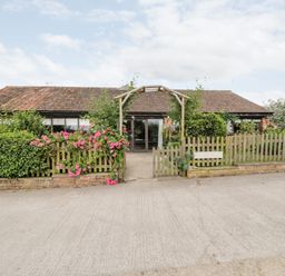 A single story building with a tiled roof and wooden fence with flowers at The Barn in Draycot Cerne near Malmesbury