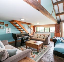 A living room with sofas a coffee table a piano and staircase at The Barn in Draycot Cerne near Malmesbury