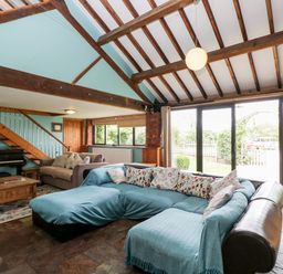 A living room with sectional sofa piano wooden coffee table and exposed beam ceiling at The Barn Draycot Cerne near Malmesbury