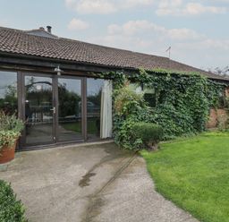 The exterior of a single-story building with large glass doors surrounded by greenery and plants at The Barn in Draycot Cerne near Malmesbury