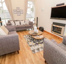 A living room with gray sofas a wall mounted TV a geometric patterned rug and round wooden coffee tables at Seion Chapel in Beaumaris