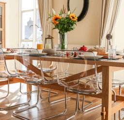 A dining room with a wooden table clear chairs a vase with flowers and tableware at Seion Chapel in Beaumaris