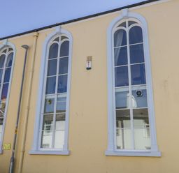 The exterior of a building with three tall arched windows and a pale yellow wall at Seion Chapel in Beaumaris