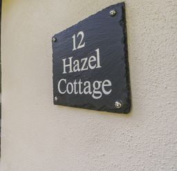 A house name plaque reading 12 Hazel Cottage on an exterior wall near a window at Hazel Cottage in Poughill near Bude