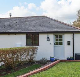 Exterior view of a single-story building with a white door window and hedges in front at Hazel Cottage in Poughill near Bude