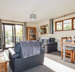 A living room with sofas a wooden dining table bookshelf and sliding glass doors at Hazel Cottage in Poughill near Bude