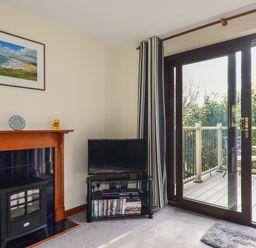 A living room corner with a black TV on a stand and a fireplace next to a sliding glass door opening to a balcony at Hazel Cottage in Poughill near Bude