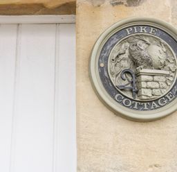 A circular plaque with an owl sculpture and the words Pike Cottage on a stone wall at Pike Cottage in Acton Turville near Chipping Sodbury