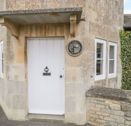 The exterior entrance door of a stone cottage with a white wooden door and two white-framed windows at Pike Cottage in Acton Turville near Chipping Sodbury