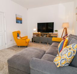 A living room with a gray sofa and yellow armchair facing a TV and wooden media console at Lyngaran House in Holyhead