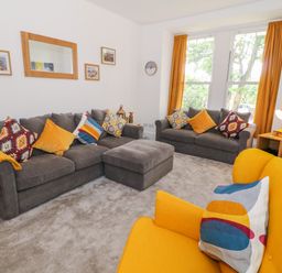 A living room with two gray sofas a yellow armchair and cushions at Lyngaran House in Holyhead