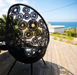 Black circular patterned outdoor chairs on a wooden deck with ocean view at Blue Bay Beach House in Mawgan Porth
