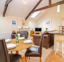A dining table with plates and glasses near a living area with leather sofas and a television at Lambkin Cottage in St Columb Major