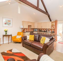 A living room with a brown leather sofa yellow cushions an orange armchair and a wooden TV stand at Lambkin Cottage in St Columb Major