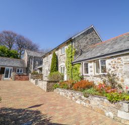 A stone house with a paved driveway and flower beds in front at Cornflower Cottage in St Columb Major
