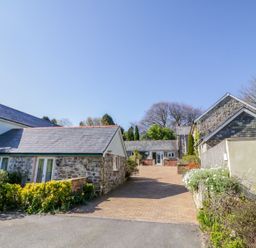 A driveway with stone buildings on both sides and plants along the edges at Cornflower Cottage in St Columb Major