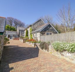 A driveway with stone cottages and a wooden fence with flowers at Cornflower Cottage in St Columb Major