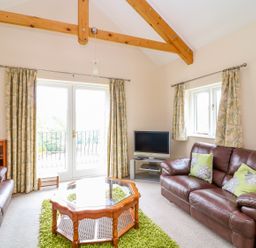 A living room with leather sofas a wooden coffee table a television and curtains at Forget-me-not in St Columb Major