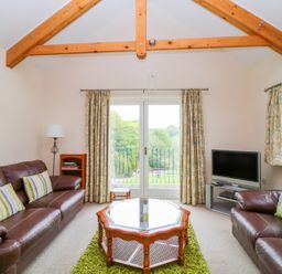 A living room with leather sofas and a coffee table facing glass doors with curtains at Forget-me-not in St Columb Major