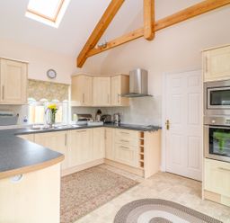 A kitchen with light wood cabinets a black countertop a skylight and exposed wooden beams at Forget-me-not in St Columb Major