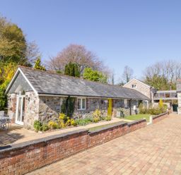 A stone cottage with a yellow door and a patio table with chairs on a paved area at FernGully in St Columb Major